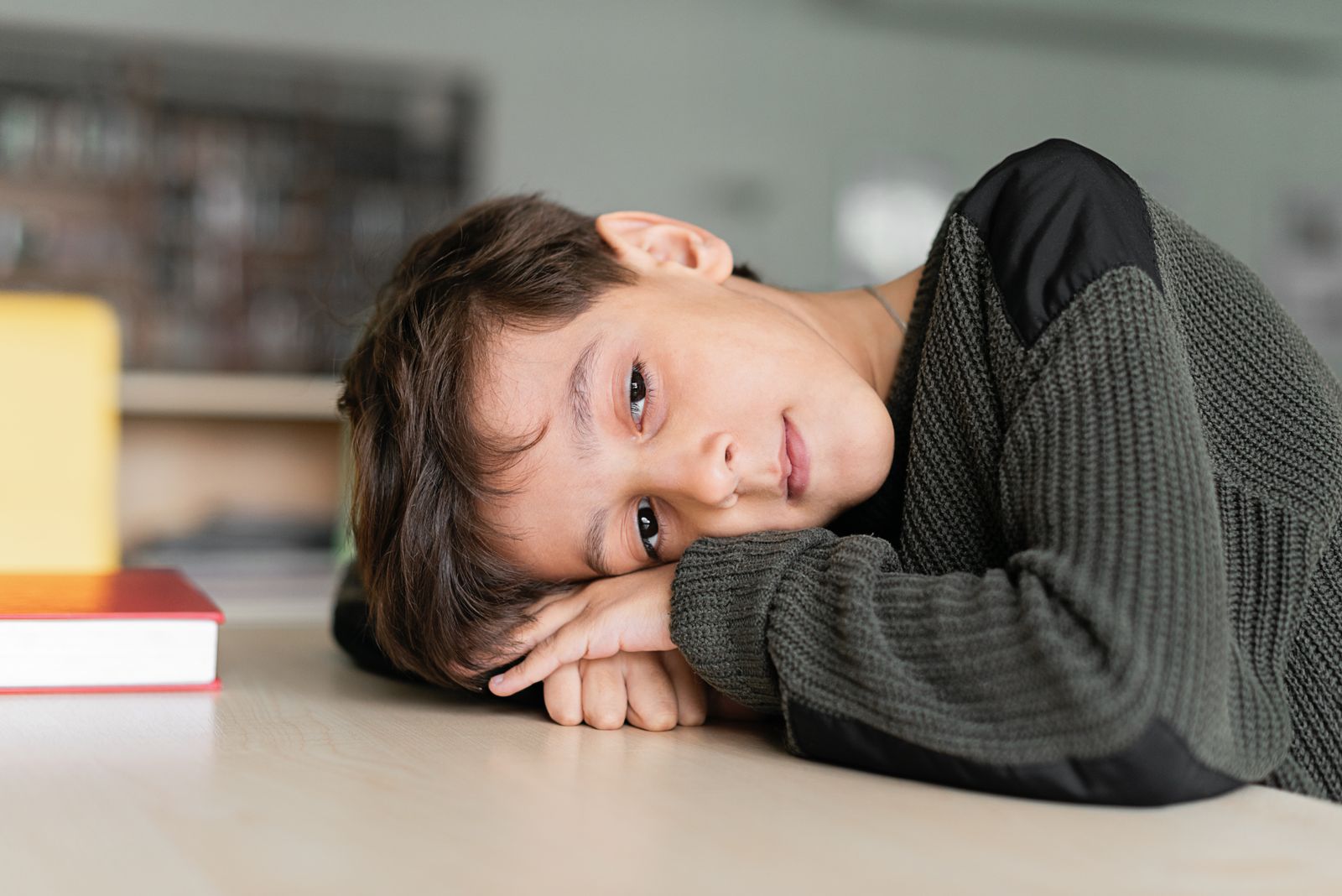 A boy lying across a desk, daydreaming instead of working