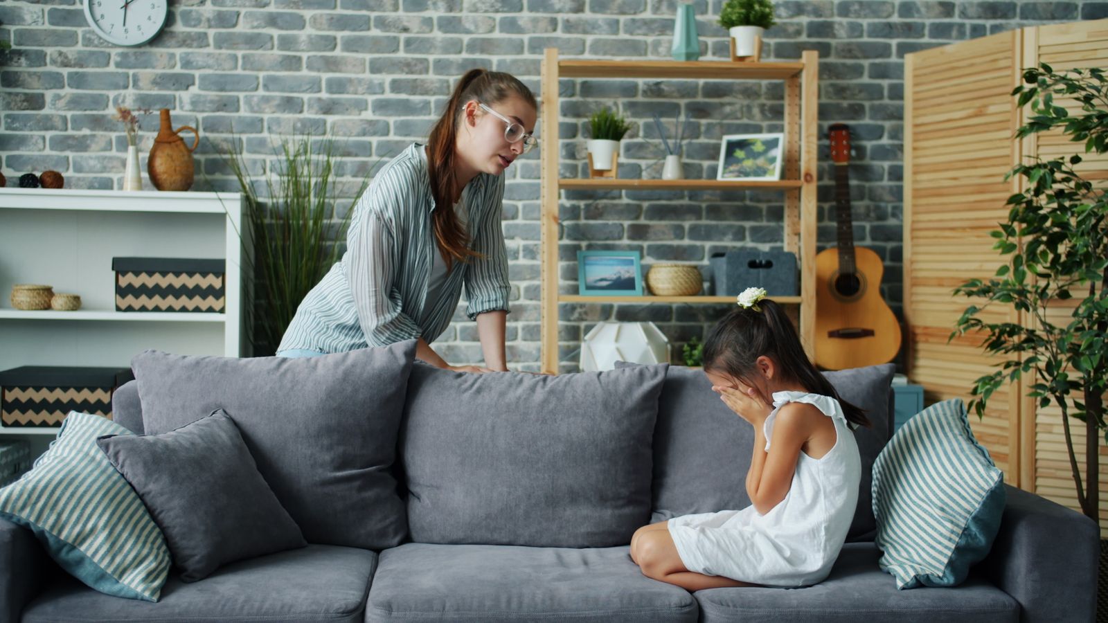 A parent coaxing a reluctant child out from behind a sofa