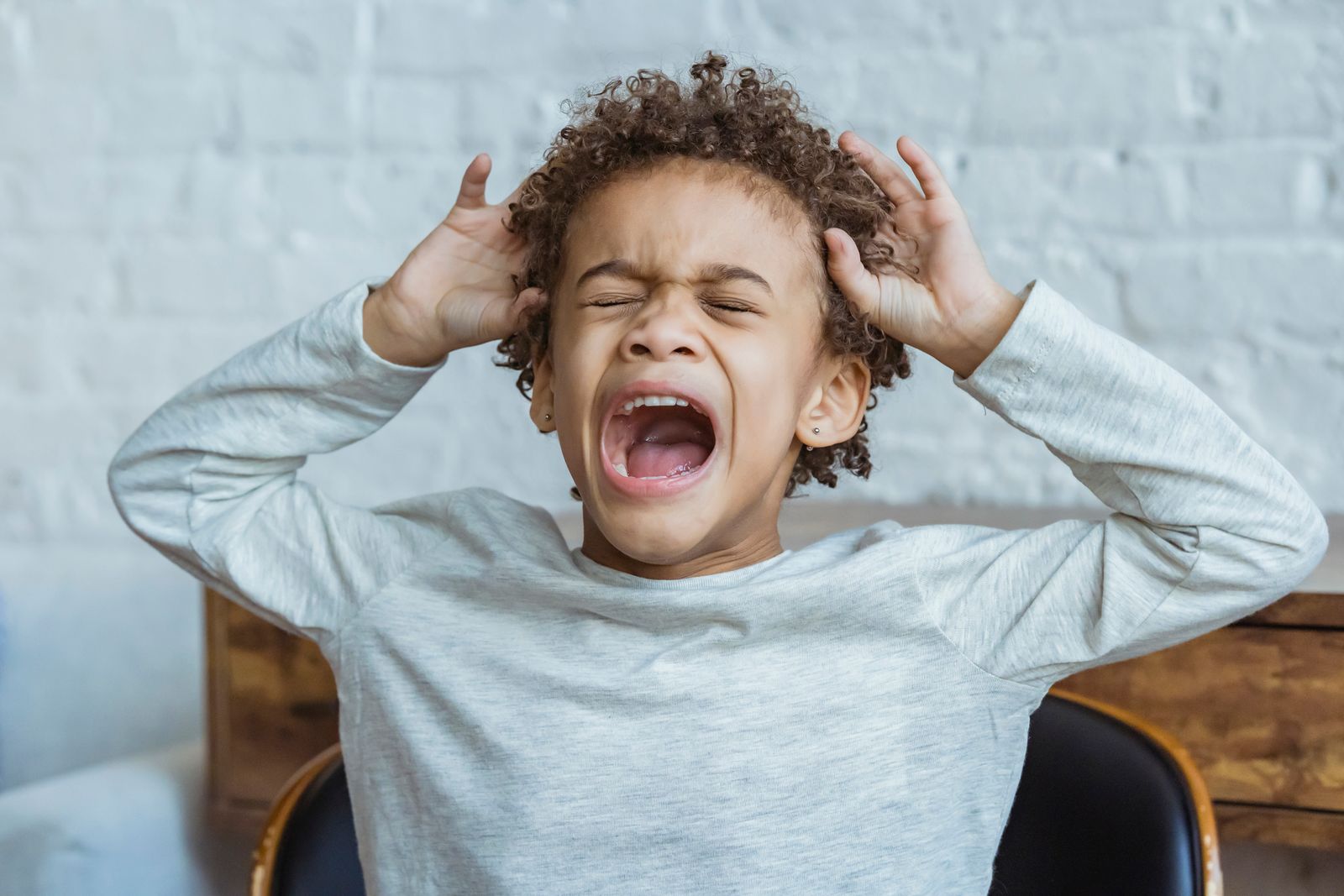 A child shouting with hands pressed to their head during a meltdown
