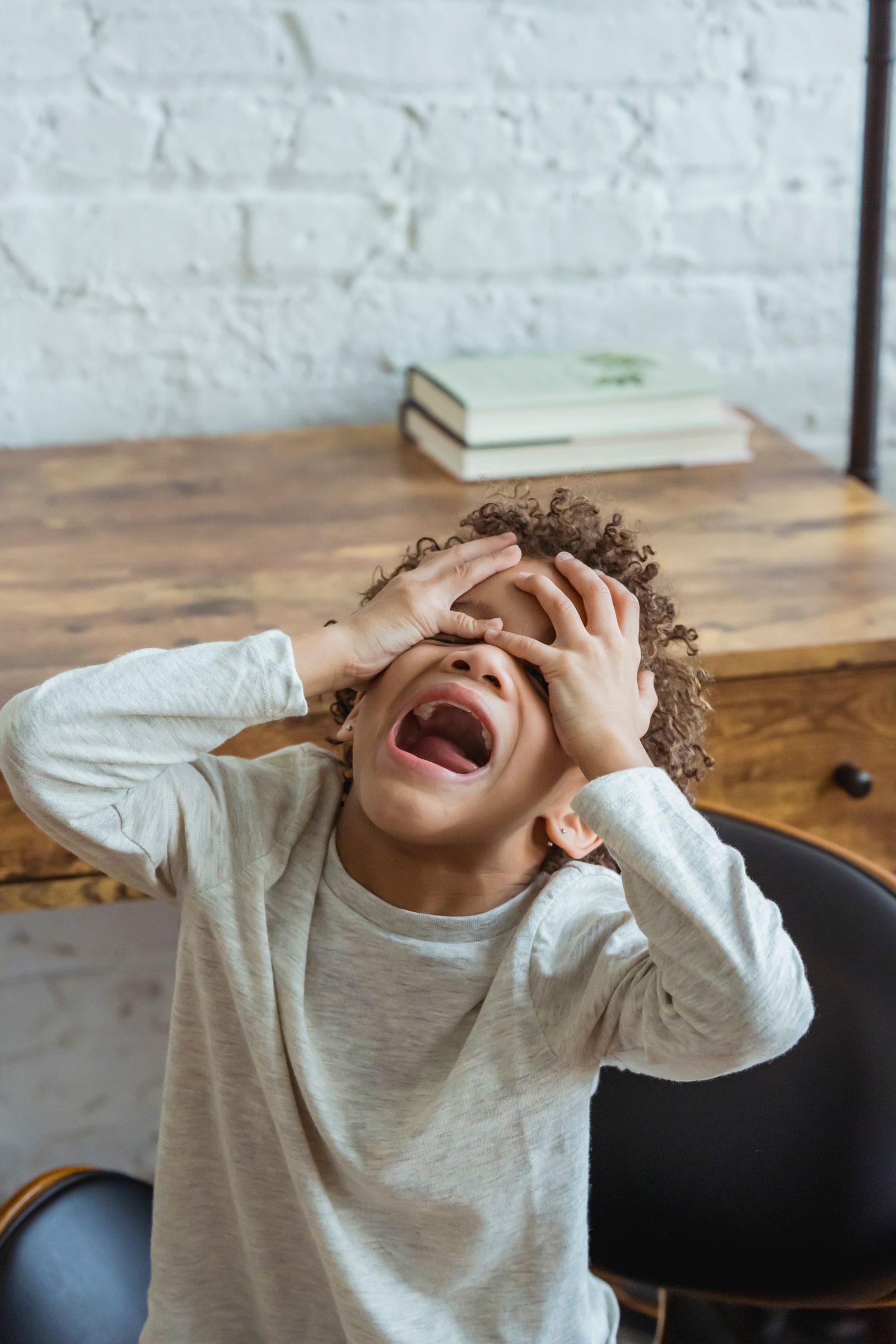 A child with hands over their face, overwhelmed at a table