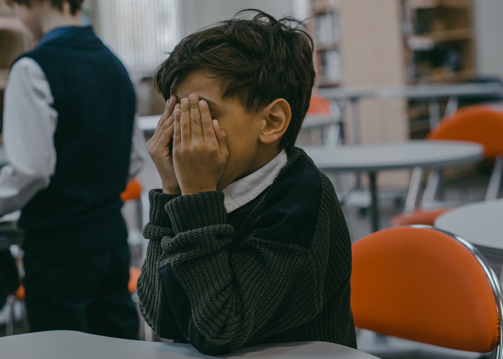 A boy covering his face at a table in a school library